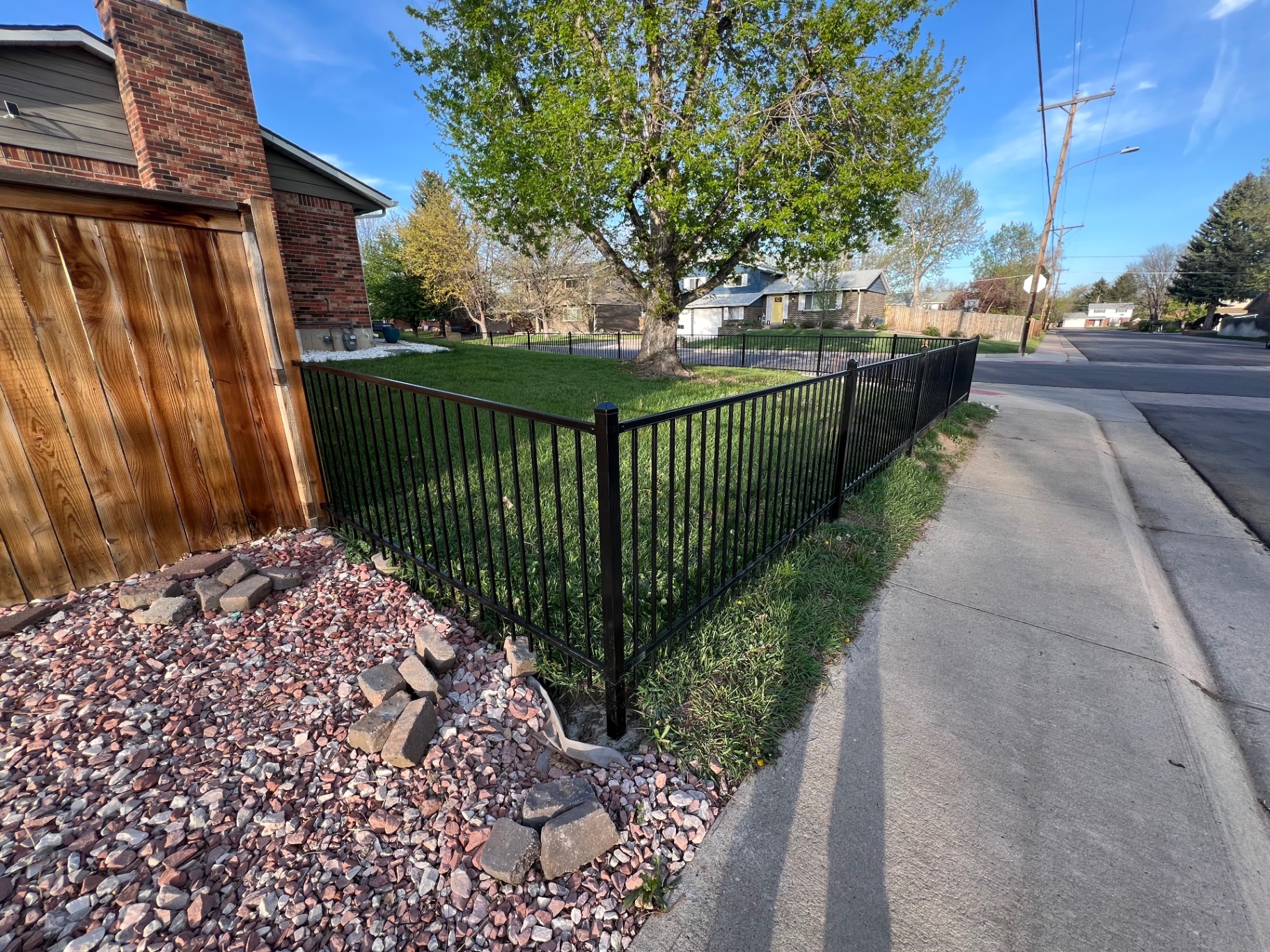 Black flat top residential ornamental iron fence wrapping a residential corner yard